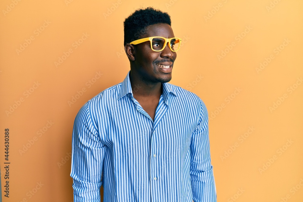 Fototapeta premium Handsome black man wearing yellow glasses looking to side, relax profile pose with natural face and confident smile.
