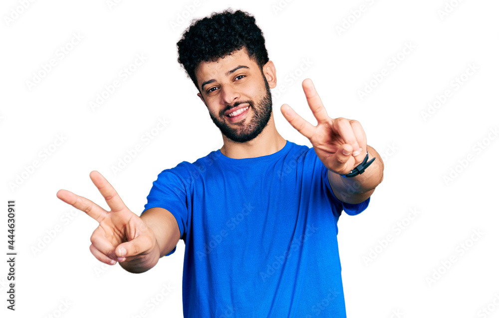 Young arab man with beard wearing casual blue t shirt smiling with tongue out showing fingers of both hands doing victory sign. number two. Young arab man with beard wearing casual blue t shirt smiling with tongue out showing fingers of both hands doing victory sign. number two.