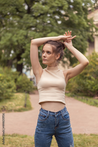 Young slender woman 18 years old stands in park with raised arms.