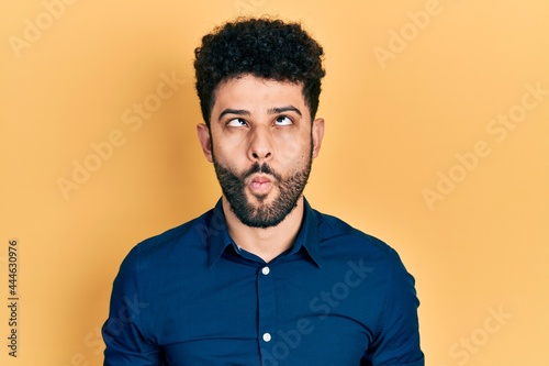 Young arab man with beard wearing casual shirt making fish face with lips  crazy and comical gesture. funny expression.
