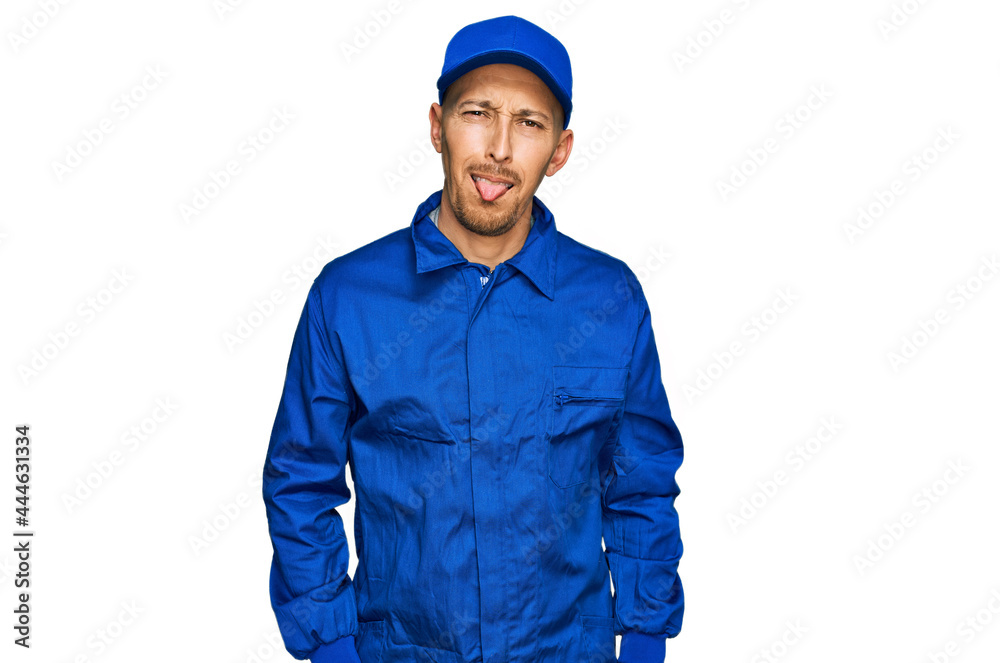 Bald man with beard wearing builder jumpsuit uniform sticking tongue out happy with funny expression. emotion concept. Bald man with beard wearing builder jumpsuit uniform sticking tongue out happy with funny expression. emotion concept.