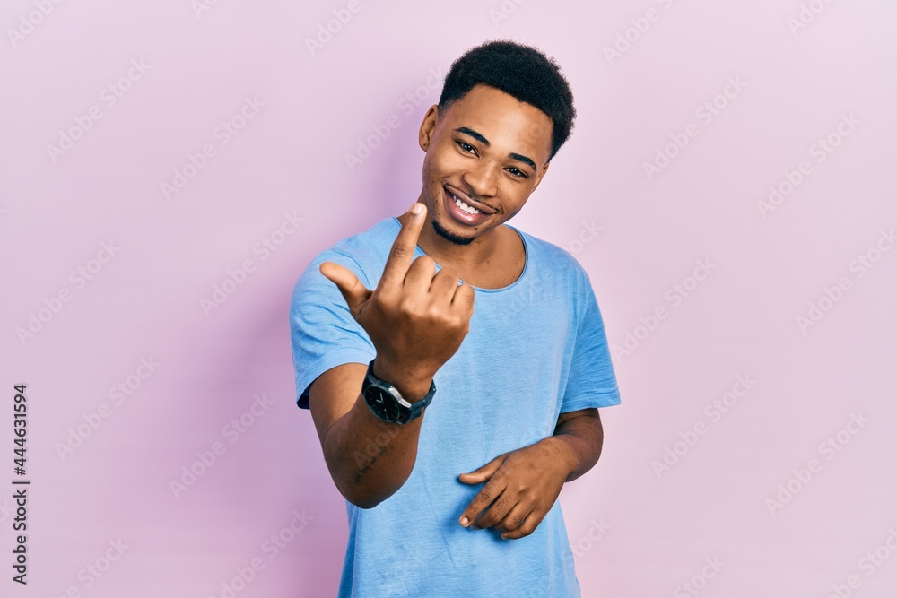 Young african american man wearing casual blue t shirt beckoning come here gesture with hand inviting welcoming happy and smiling Young african american man wearing casual blue t shirt beckoning come here gesture with hand inviting welcoming happy and smiling
