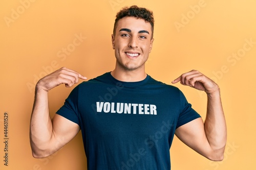 Hispanic young man wearing volunteer t shirt looking confident with smile on face, pointing oneself with fingers proud and happy.