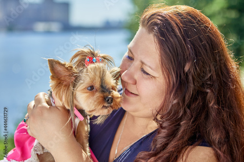 Large Build Caucasian woman is holding Yorkshire Terrier dog in her arms.