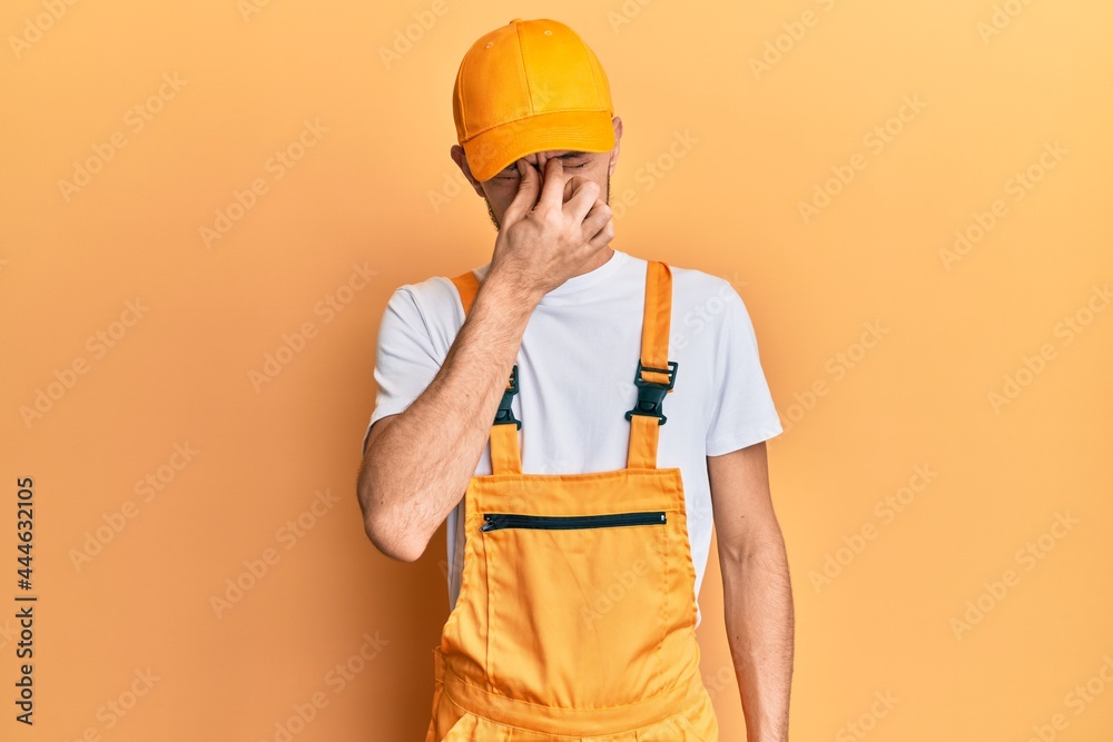 Hispanic young man wearing handyman uniform tired rubbing nose and eyes feeling fatigue and headache. stress and frustration concept. Hispanic young man wearing handyman uniform tired rubbing nose and eyes feeling fatigue and headache. stress and frustration concept.