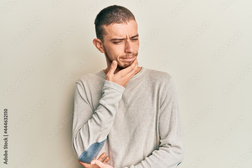 Hispanic young man wearing casual winter sweater thinking concentrated about doubt with finger on chin and looking up wondering