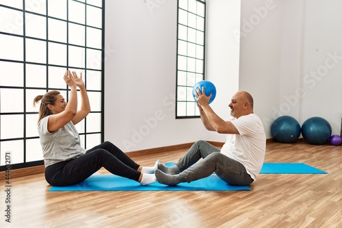 Middle age hispanic couple training passing ball at sport center.