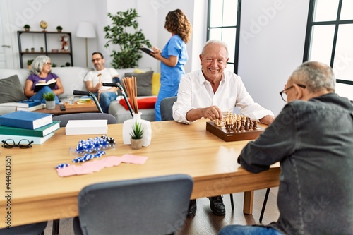 Two retired man smiling happy playing chess at nurse home.