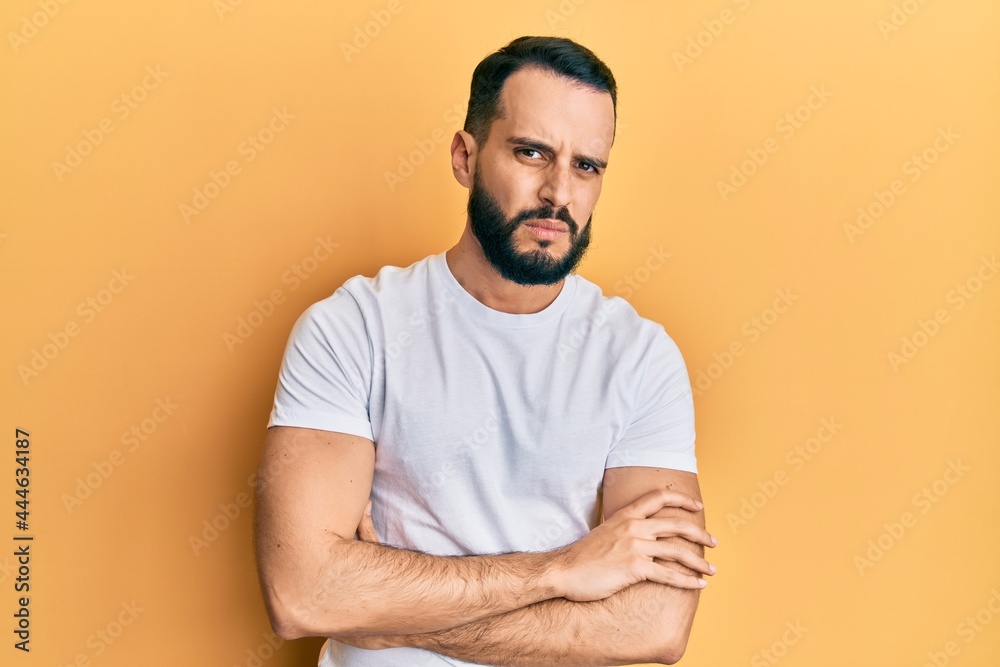 Young man with beard wearing casual white t shirt skeptic and nervous, disapproving expression on face with crossed arms. negative person. Young man with beard wearing casual white t shirt skeptic and nervous, disapproving expression on face with crossed arms. negative person.