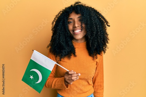 African american woman with afro hair holding pakistan flag looking positive and happy standing and smiling with a confident smile showing teeth