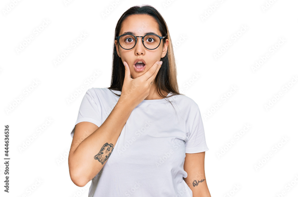 Young hispanic woman wearing casual white t shirt looking fascinated with disbelief, surprise and amazed expression with hands on chin