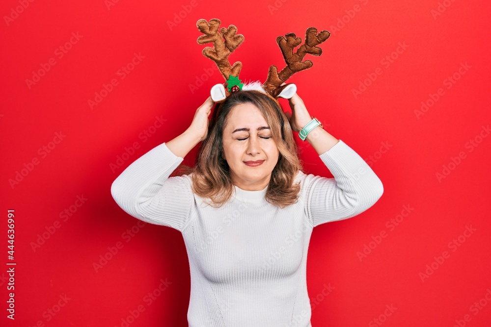 Middle age caucasian woman wearing cute christmas reindeer horns suffering from headache desperate and stressed because pain and migraine. hands on head. Middle age caucasian woman wearing cute christmas reindeer horns suffering from headache desperate and stressed because pain and migraine. hands on head.
