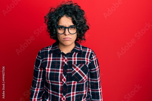 Young hispanic woman with curly hair wearing casual clothes and glasses skeptic and nervous, frowning upset because of problem. negative person.