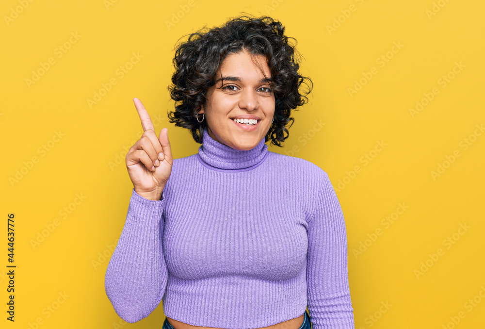 Young hispanic woman with curly hair wearing casual clothes pointing finger up with successful idea. exited and happy. number one. Young hispanic woman with curly hair wearing casual clothes pointing finger up with successful idea. exited and happy. number one.