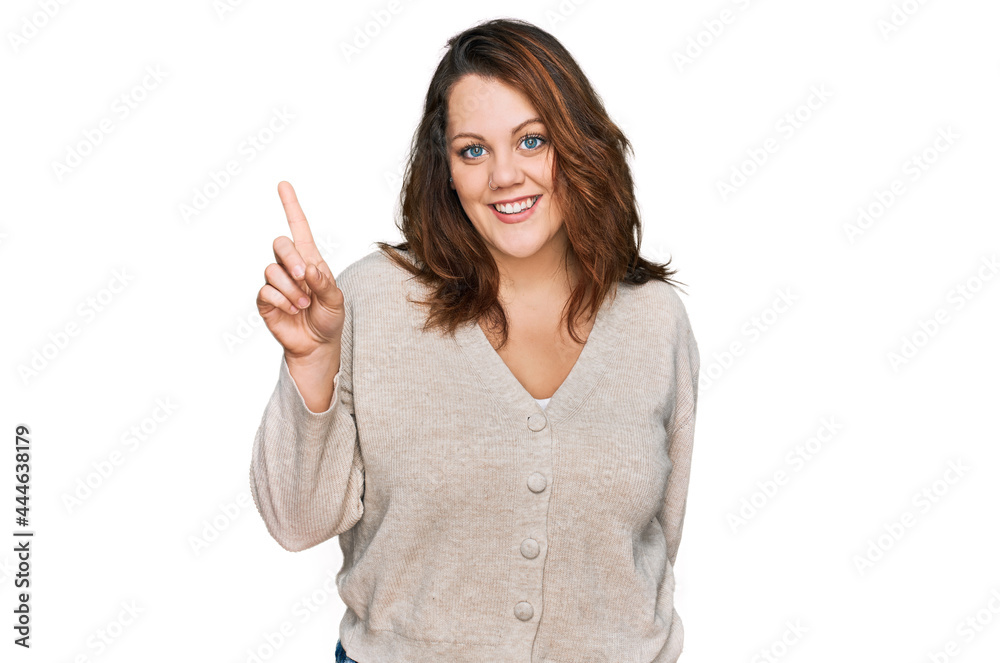 Young plus size woman wearing casual clothes showing and pointing up with finger number one while smiling confident and happy. Young plus size woman wearing casual clothes showing and pointing up with finger number one while smiling confident and happy.