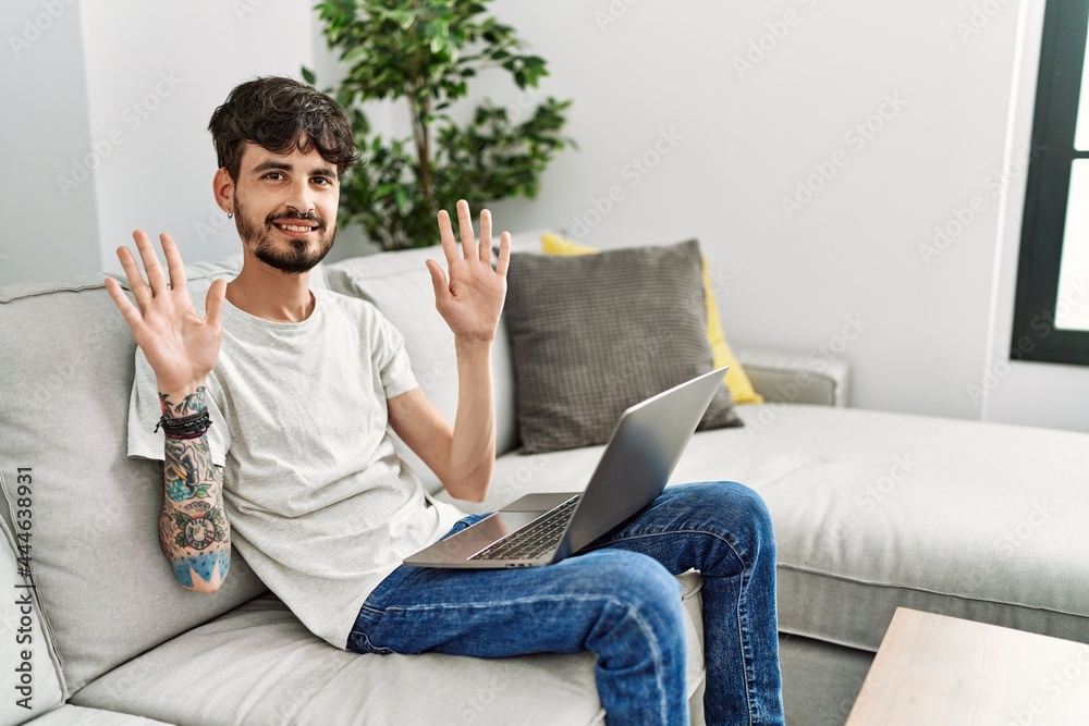 Hispanic man with beard sitting on the sofa showing and pointing up with fingers number ten while smiling confident and happy. Hispanic man with beard sitting on the sofa showing and pointing up with fingers number ten while smiling confident and happy.