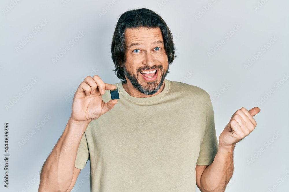 Middle age caucasian man holding sdxc card pointing thumb up to the side smiling happy with open mouth Middle age caucasian man holding sdxc card pointing thumb up to the side smiling happy with open mouth