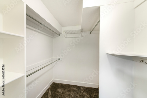 Interior of a plain white walk in closet with shelvings and carpeted floor