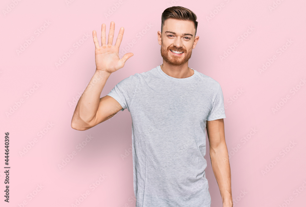Young redhead man wearing casual grey t shirt showing and pointing up with fingers number five while smiling confident and happy. Young redhead man wearing casual grey t shirt showing and pointing up with fingers number five while smiling confident and happy.