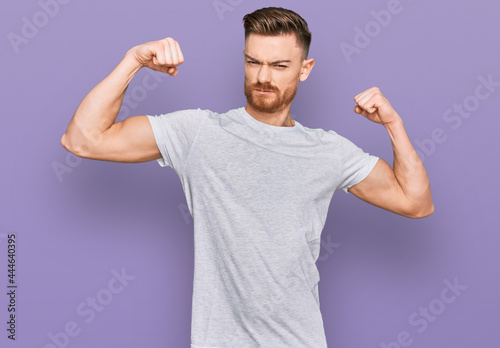 Young redhead man wearing casual grey t shirt showing arms muscles smiling proud. fitness concept.