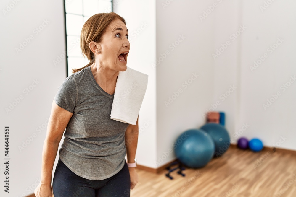 Middle age woman wearing sporty look training at the gym room angry and mad screaming frustrated and furious, shouting with anger. rage and aggressive concept. Middle age woman wearing sporty look training at the gym room angry and mad screaming frustrated and furious, shouting with anger. rage and aggressive concept.