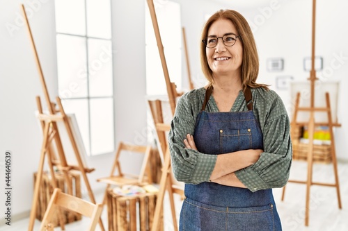 Middle age artist woman smiling happy standing with arms crossed gesture at art studio.