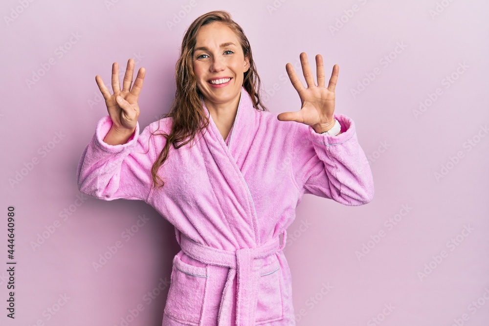 Young blonde woman wearing bathrobe showing and pointing up with fingers number nine while smiling confident and happy. Young blonde woman wearing bathrobe showing and pointing up with fingers number nine while smiling confident and happy.