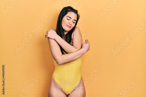 Young hispanic girl wearing swimsuit hugging oneself happy and positive, smiling confident. self love and self care
