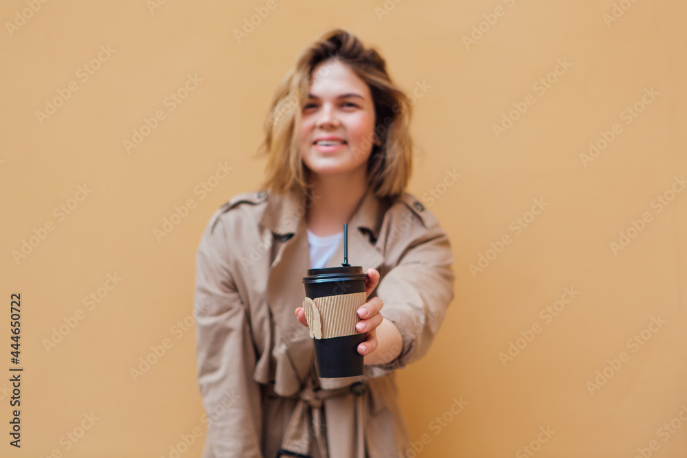 Young millennial woman with wild hair dressed in an autumn coat standing a cup of coffee to go near the wall. Young millennial woman with wild hair dressed in an autumn coat standing a cup of coffee to go near the wall.