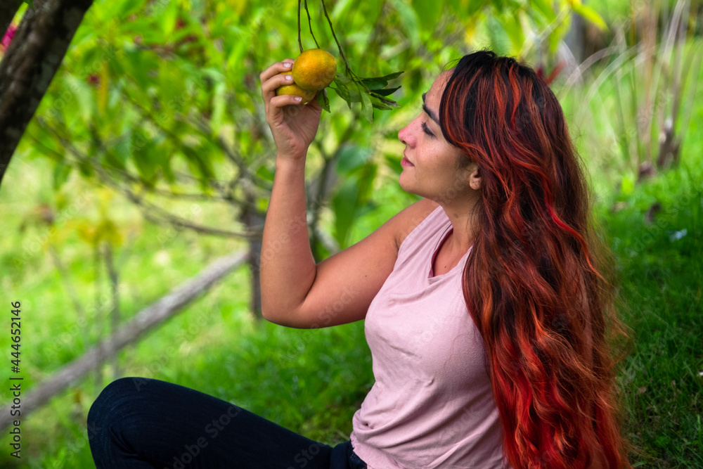 Red haired woman taking an orange straight from the tree