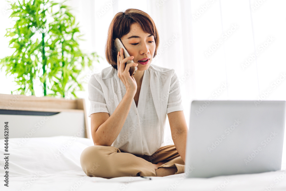 Young smiling happy beautiful asian woman relaxing using laptop computer in the bedroom at home.Young creative girl working and typing on keyboard.work from home concept Young smiling happy beautiful asian woman relaxing using laptop computer in the bedroom at home.Young creative girl working and typing on keyboard.work from home concept