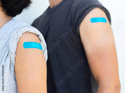 Vaccinations, bandage plaster on vaccinated people concept. Blue adhesive bandages on a woman's shoulder who wearing grey shirt next to a man in dark shirt, after vaccination treatment.