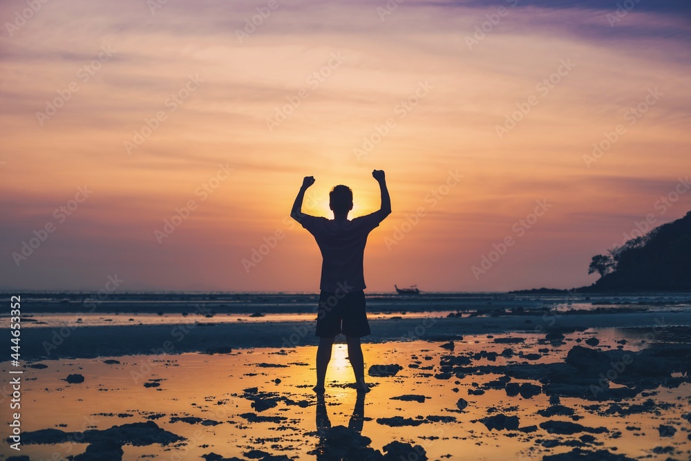 Asian man standing on the beach by the sea at morning sky with sunrise background.