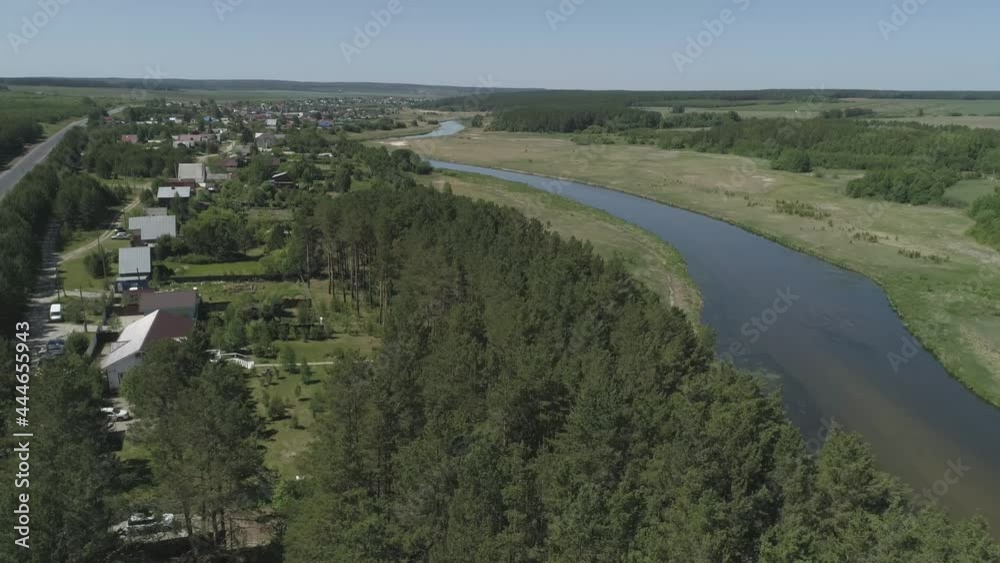 Aerial view of private houses in the forest next to the river. Nearby there is a road. Picturesque residential area. Summer sunny day.
