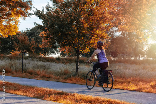 Adventurous White Caucasian Adult Woman riding a road bicycle on a bike path at the famous Stanley Park in a modern city. Sunset. Fall Colors Art Render. Downtown Vancouver, British Columbia, Canada.
