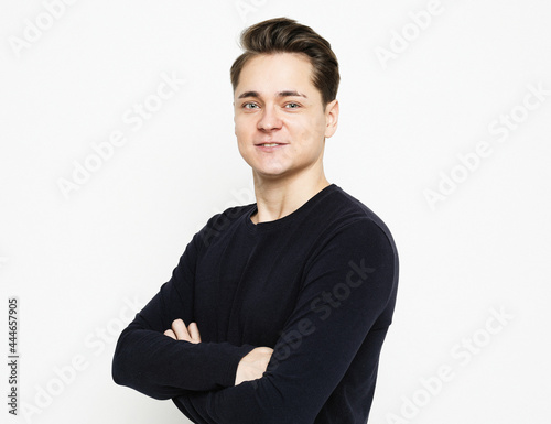 Young handsome man wearing black sweater crossing hands and look at camera over white background