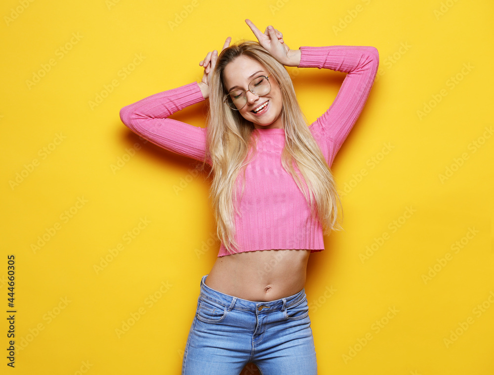 Young woman wearing casual wear over yellow background doing funny gesture with finger over head as bull horns Young woman wearing casual wear over yellow background doing funny gesture with finger over head as bull horns