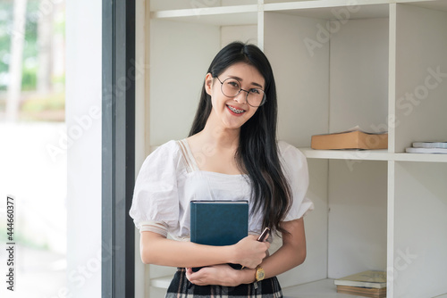 Free Download Young Asian woman wearing glasses Beautiful smile standing holding a book. Looking at the camera. - GFXLoad