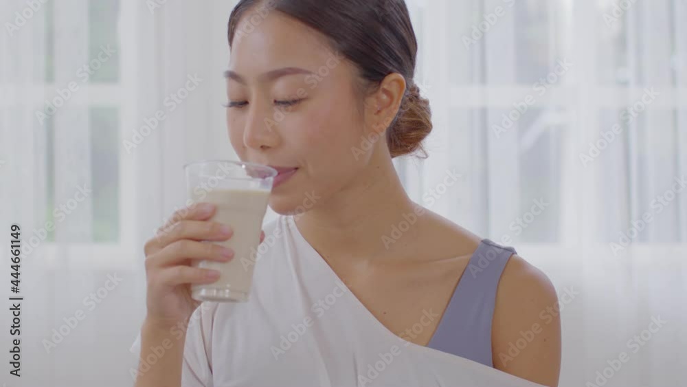 Healthy Young Asian woman Drinking milk with calcium for strong bone at home,Smiling indian woman holding soy milk on glass enjoy with nutrition wellness life,Wellness with natural milk fresh Concept