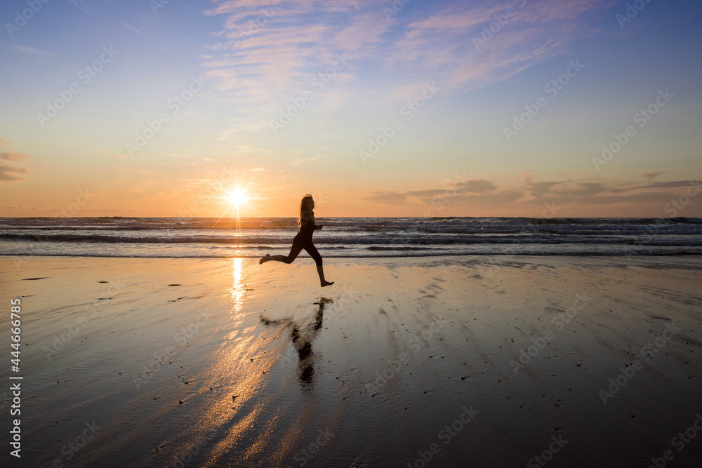 young girl running and jumping with happiness on the beach at sunset