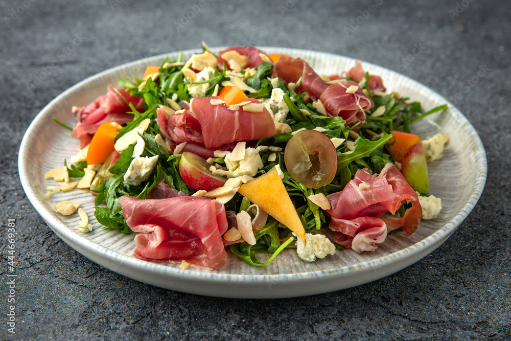 Salad with prosciutto, persimmon, almonds and dor blue cheese. Ready menu for the restaurant. Neutral gray blue textured background