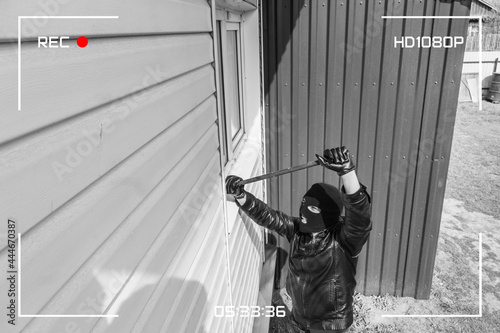 Protection of a private residential building with the help of an external video surveillance system. CCTV view of burglar breaking in to home through window with crowbar. black and white style