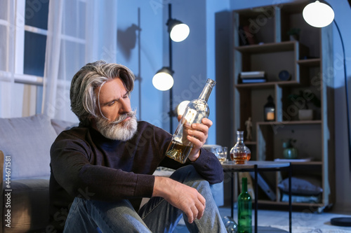 Senior man with bottle of drink late in evening at home