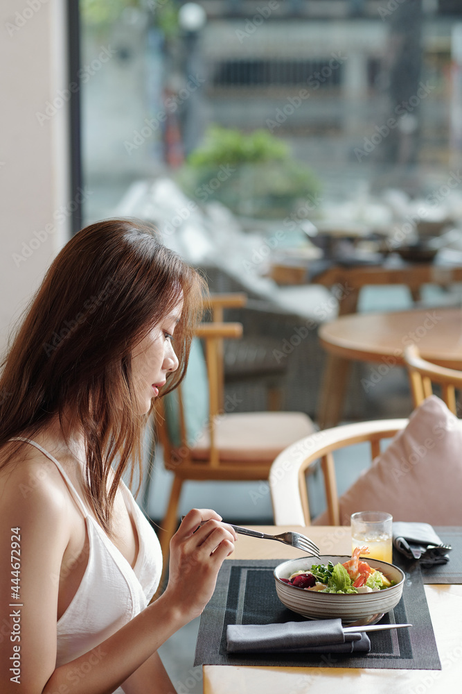 Pretty young woman enjoying delicious salad for lunch in cafe