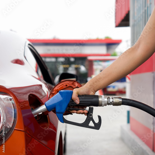 Gas station worker's hand holding blue benzene gas pump, filling up red sport car tank. Close up