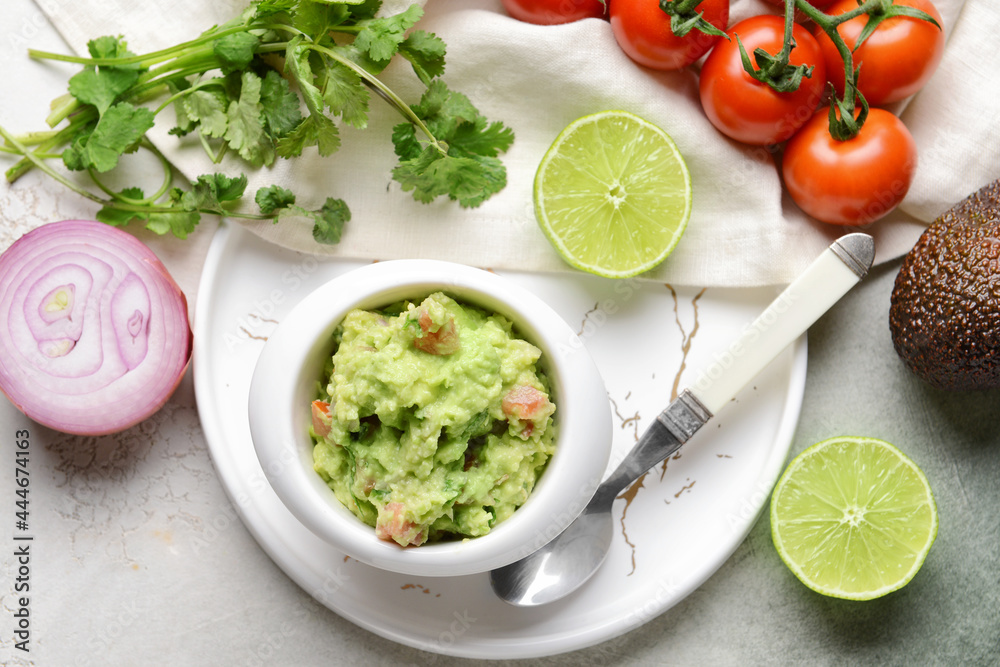 Bowl with tasty guacamole, lime, tomato and onion on light background
