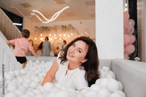 an attractive woman in white clothes lies in a dry pool with white balls. photo