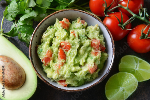 Bowl with tasty guacamole, avocado and lime on dark background, closeup
