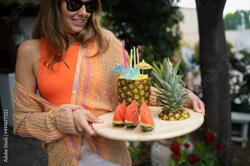 Young woman on vacation holding a tray with fruits such as watermelon and pineapple with straw on it. Summer healthy fruit concept. © Lomb