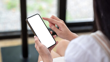 Back view of woman holding a smartphone blank white screen sitting in a chair.